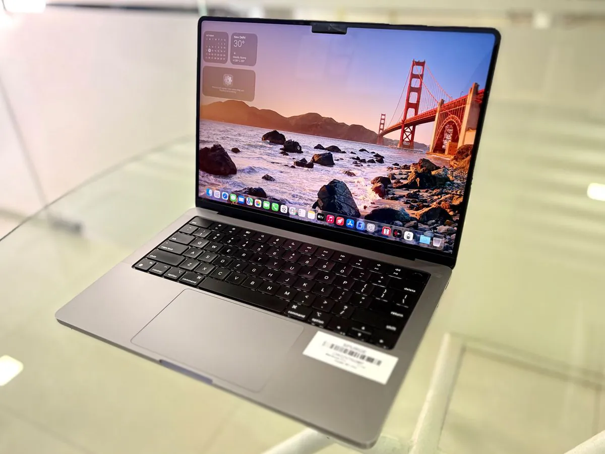MacBook Pro 14-inch M1 Pro in Silver from a right three-quarter angle, open with the display on and the SPURGE asset label on the palm rest