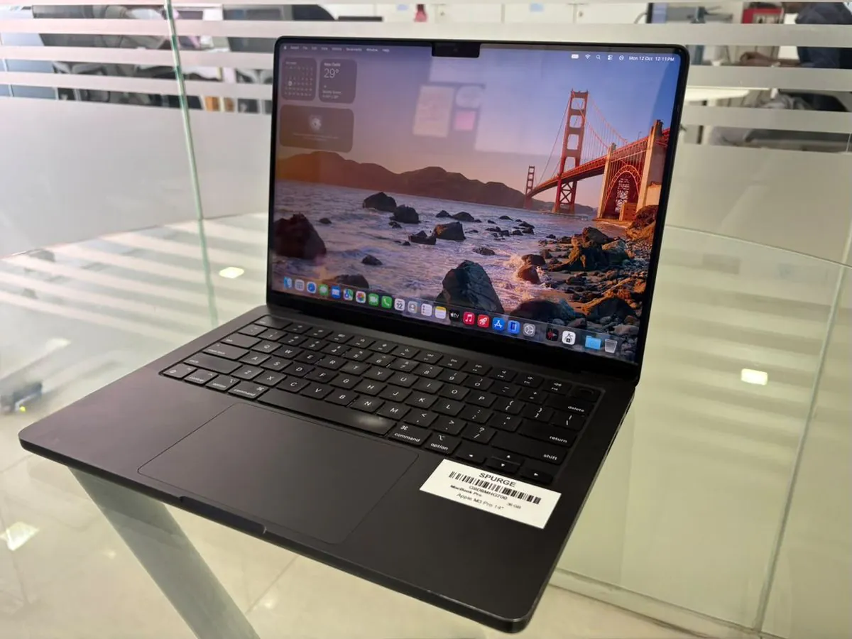 MacBook Pro 14-inch M3 Pro from a right three-quarter angle, open with the display on and the SPURGE asset label on the palm rest