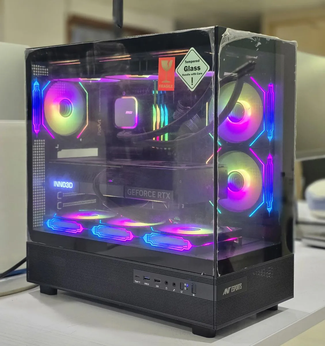 ASUSTeK Pro PC Z890 Creator WiFi in an Ant Esports tempered-glass case, three-quarter view showing the front USB-C, two USB-A and audio ports, RGB fans, an MSI liquid cooler and an Inno3D GeForce RTX graphics card